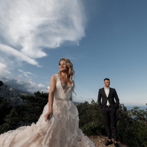 Happy bride and groom on a high rock against the background of the sea sunset A beautiful bride and groom on their wedding day walk along the rocky coast by the sea.Young couple in the mountains in spring, honeymoon,happy smiling bride and groom spend time together in the mountainous area near the ocean.Wedding day.Honeymoon.