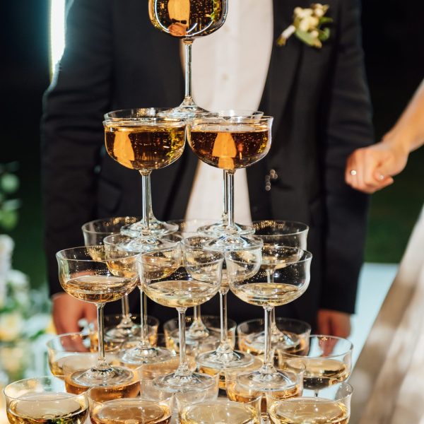 A large pyramid of champagne glasses at the evening ceremony at the arch. In the background, the bride and groom are hugging.